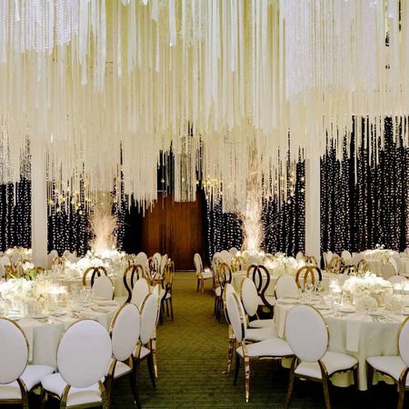 White and gold table settings with fringes as ceiling decor.