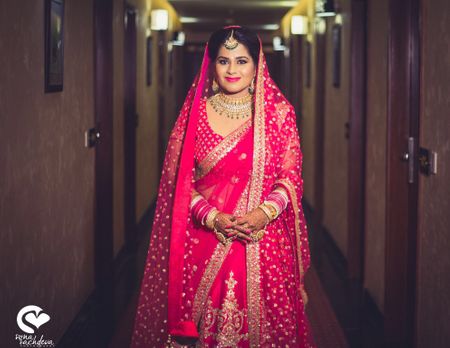 Bride in raspberry pink lehenga with contrasting green jewellery