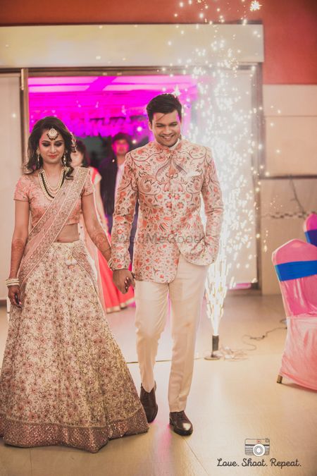 Coordinated bride and groom in light peach and off white floral embroidered lehenga and jacket