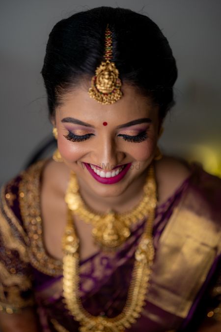 South Indian bride wearing aubergine saree with temple jewels.