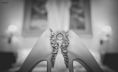 Black and white photo of ring between bridal shoes