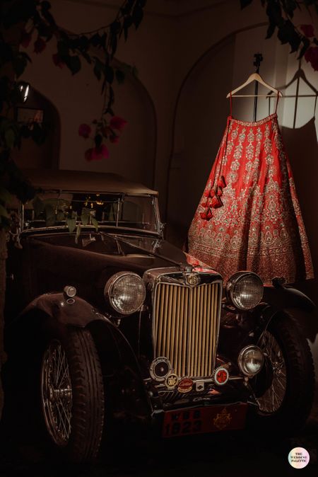 red bridal lehenga on hanger next to a vintage car