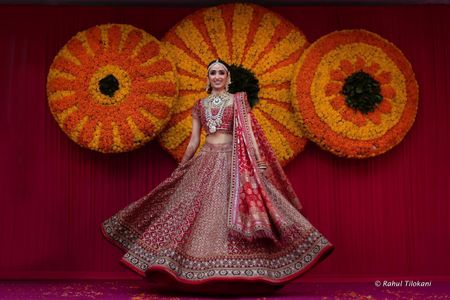 Photo of Gorgeous bride twirling in a heavy red lehenga and layered jewelry
