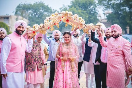Sikh bride in light pink entering under unique phoolon ki chadar