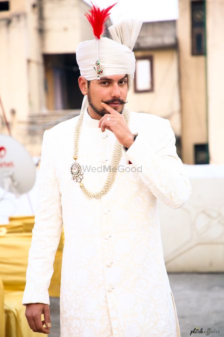 Groom wearing white sherwani jewellery and turban with red feather