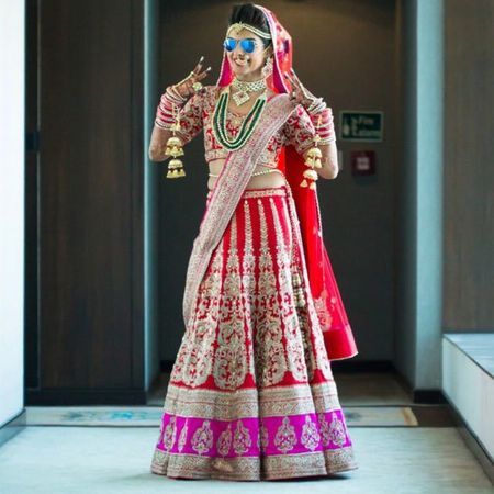 Photo of Bride in red and pink bridal lehengas wearing reflectors
