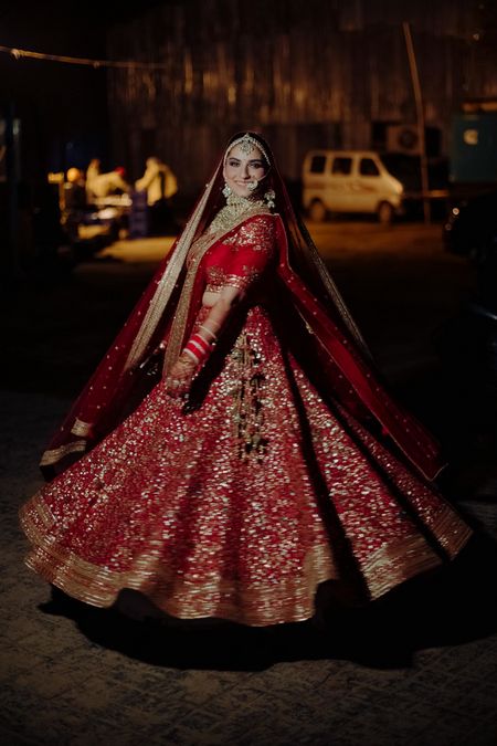 Bride twirling around in her red and gold lehenga.
