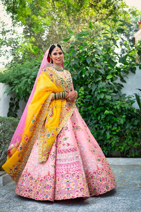 Bride wearing a pastel pink lehenga with a yellow dupatta and emerald jewellery.
