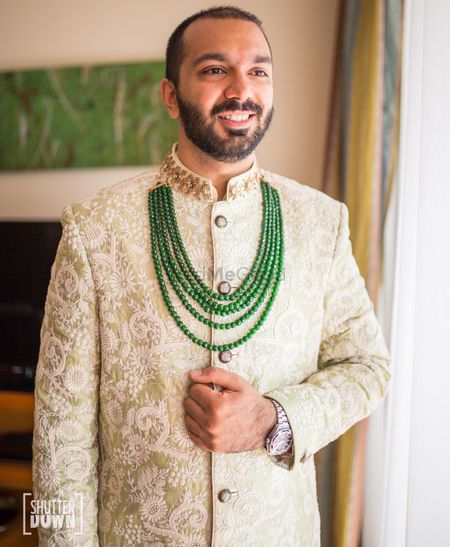 Groom wearing light green sherwani with contrasting necklace