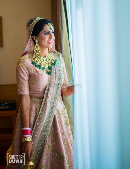 Bride looking out of window in pink lehenga with green jewellery