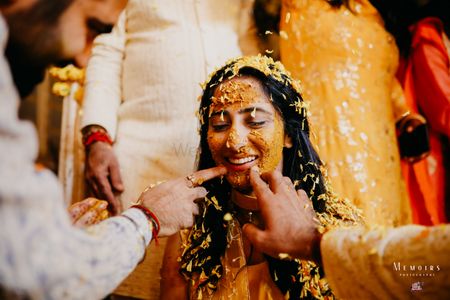 Bride smiling while getting smeared with Haldi.
