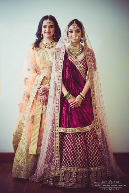 Bride with sister wearing maroon bridal lehenga 