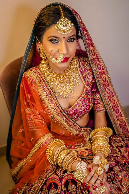 A bride in a multicolored lehenga with heavy gold jewellery