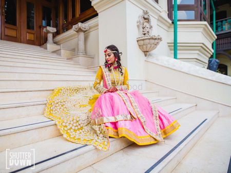 Bride sitting on stairs in light pink and yellow mehendi lehenga
