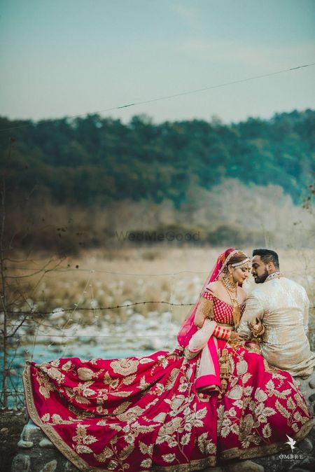 Photo of Bride and groom couple portrait in red bridal lehenga in outdoor location