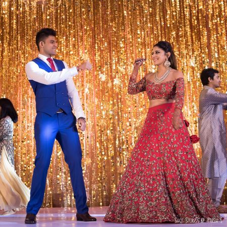 Photo of Sangeet dance for bride and groom with gold stage backdrop