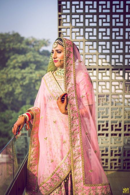 Photo of Stunning pastel pink bridal lehenga with gold work and a unique dupatta drape in triangle