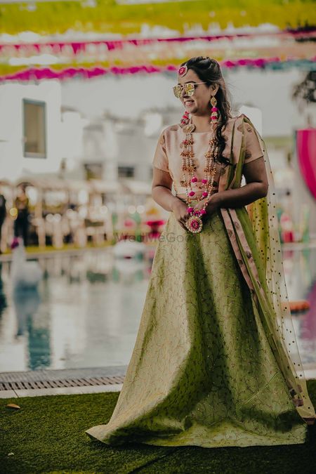 A bride-to-be in a green lehenga and pink floral jewellery for her mehndi 
