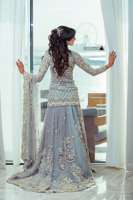 Bridal back shot in ice blue lehenga posing against window