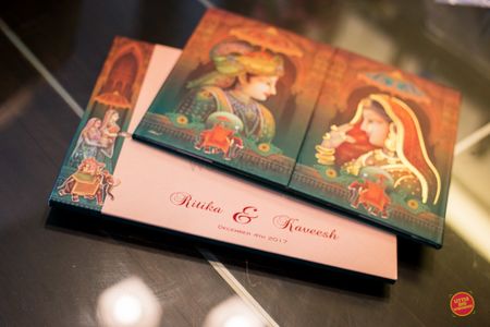 Photo of Modern Mughal theme wedding card with bride and groom portraits