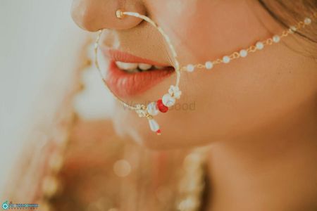 A bride in a nath with red and white beads. 