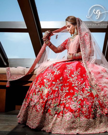 Photo of A bride in red and pink lehenga poses with a ghunghat.