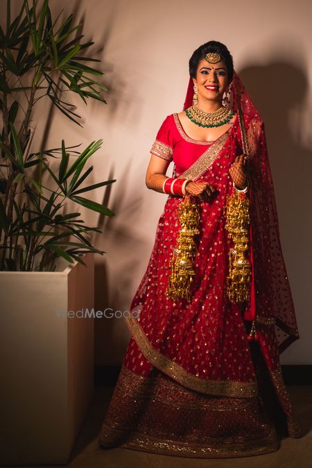 A bride in a red lehenga and gold kaleera smiles for the camera