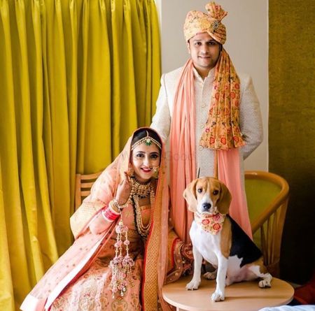 A bride and groom in coordinated outfits pose with a dog