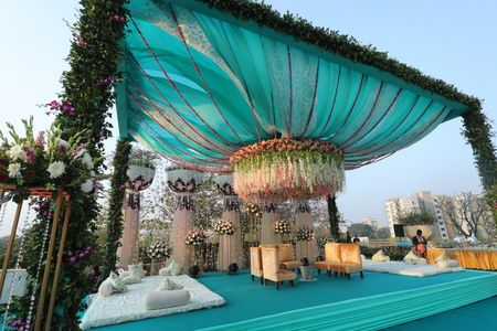 Turquoise mandap with a huge floral chandelier in the centre.