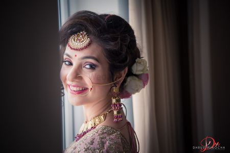 A bride smiles as she gets ready, wearing a maang tika and a floral bun