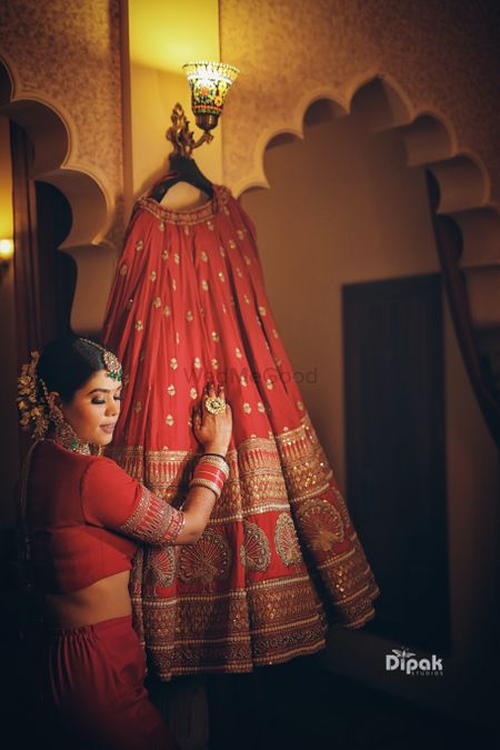 Bride posing with red lehenga on hanger 