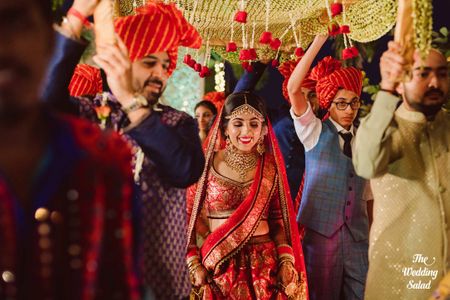 Bride in red entering under gold phoolon ki chadar 