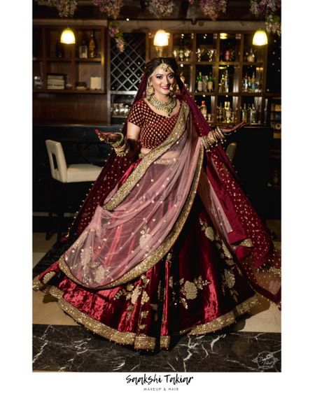 A bride in maroon lehenga and double dupatta twirling