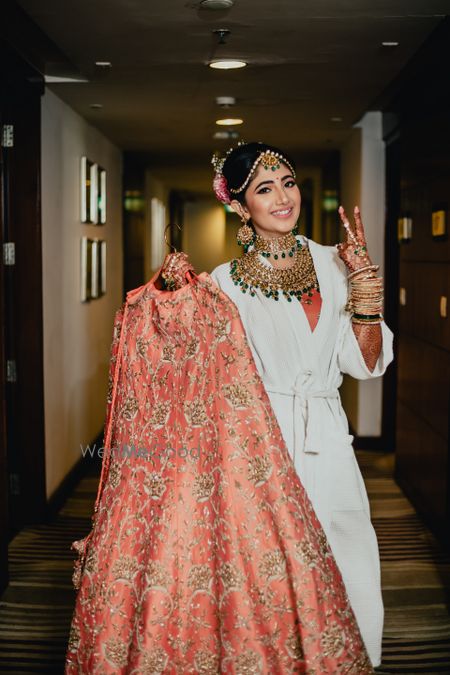 Bride in robe holding peach lehenga 