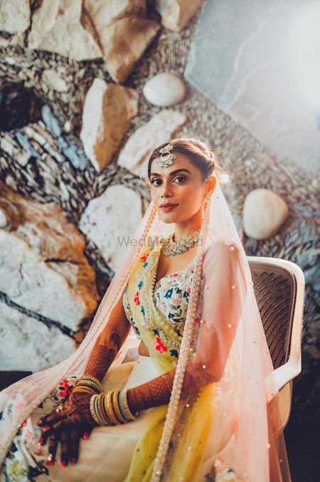 Bride dressed in an ivory lehenga with peach and yellow dupattas.