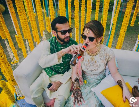 Photo of A groom to be helps his to be bride with a drink on her mehendi day