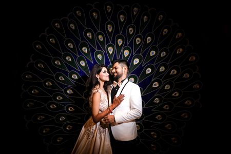 Sangeet couple shot against peacock backdrop 