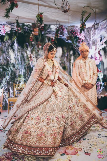 A bride in creme lehenga twirls as her groom looks on