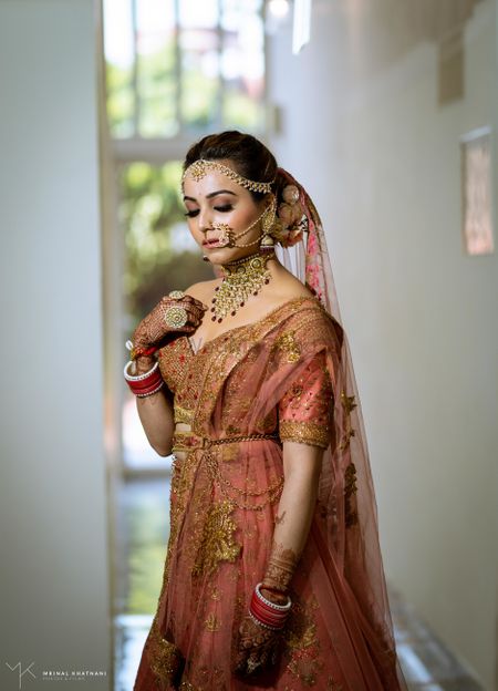A beautiful bride in a stunning peach lehenga with marvellous gold jewellery. 