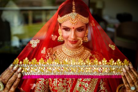 Bride holding her red and gold dupatta as a veil
