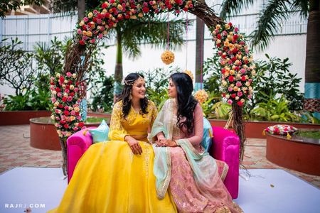 Bride with sister on arch bridal seat on mehendi 