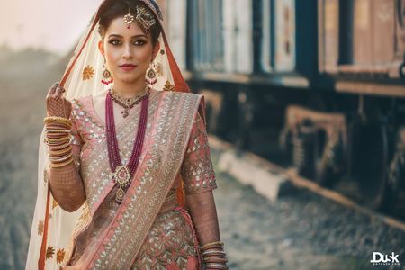 A bride in a pink lehenga and contrasting maroon colored jewels