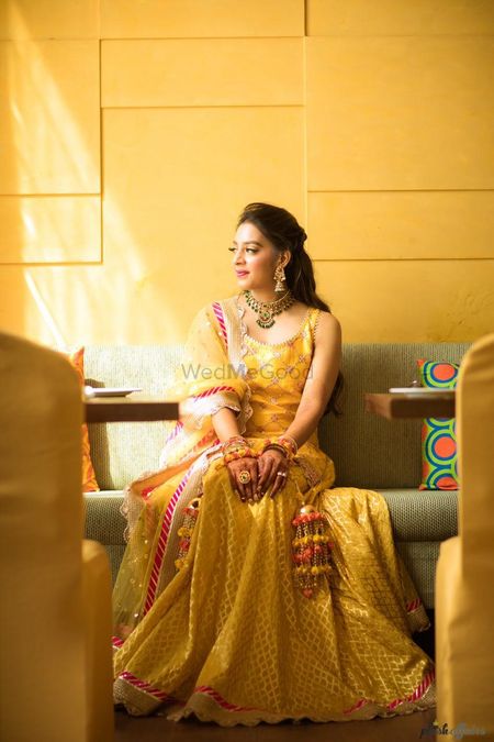 A bride in a yellow outfit and pompom kaleere for her mehndi