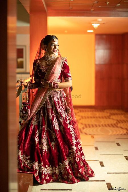 A bride in a red lehenga with a shell pink dupatta and potli