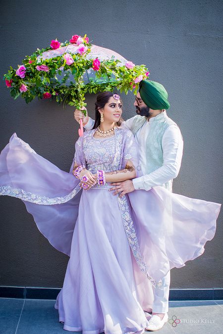 Photo of A couple pose with a floral umbrella on their mehndi