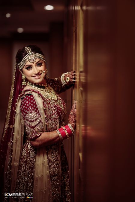 A bride in a maroon lehenga posing on her wedding day