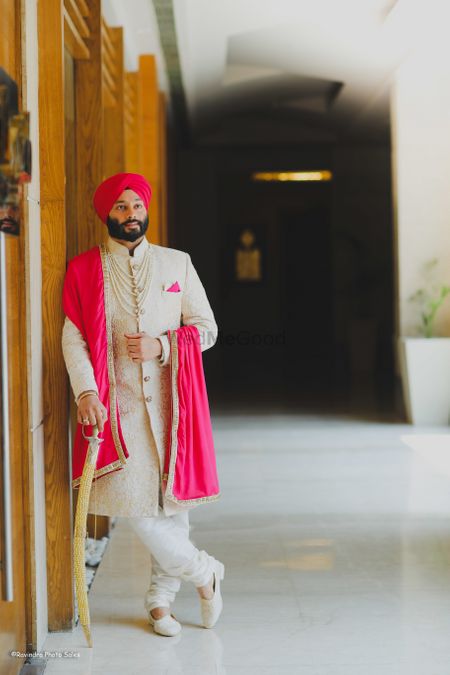 A groom in a stunning off-white embroidered sherwani coupled with bright pink dupatta and turban. 