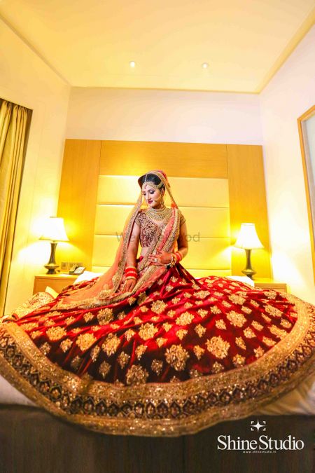 Photo of Bride sitting on hotel bed with flared out maroon velvet lehenga