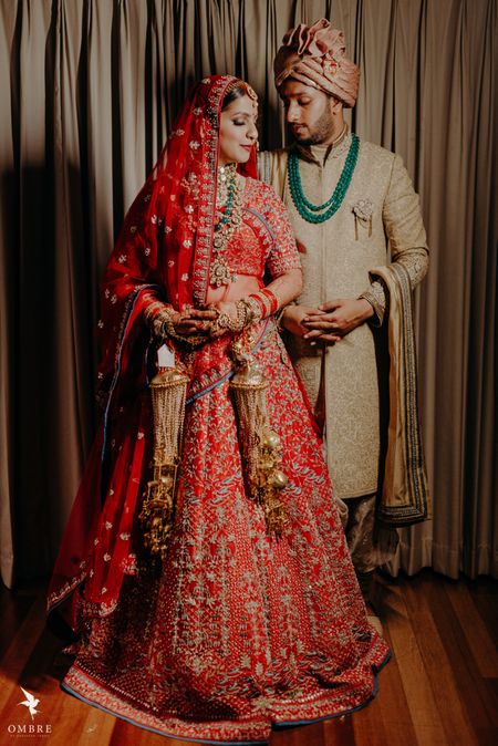 bride in red and groom in beige with a green necklace 