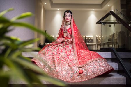 Photo of bride sitting on stairs showing off bright red lehenga